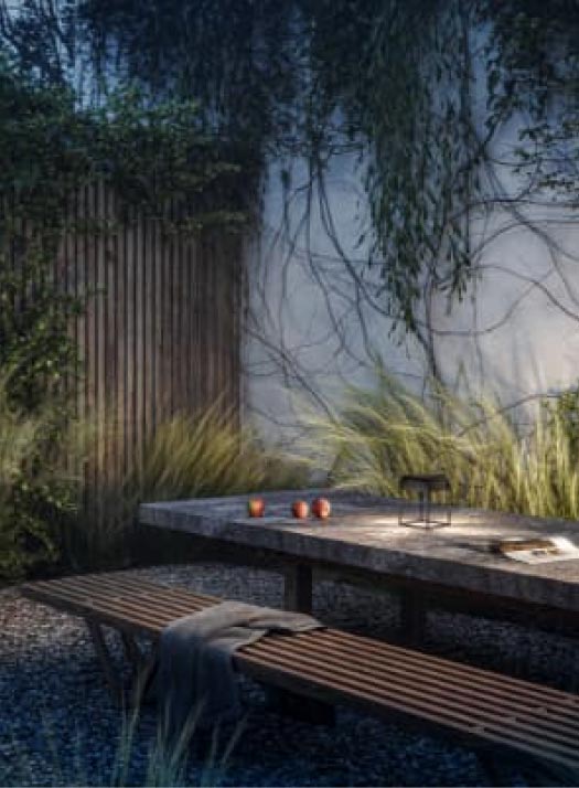 Ein moderner Essbereich im Freien mit handwerklich inspirierten Gartenmöbeln: eine Holzbank und ein Steintisch mit drei Tassen und einer Laterne, umgeben von hohem Gras, Kletterpflanzen und einem Holzzaun im klassischen Garten- und Landschaftsbaustil.