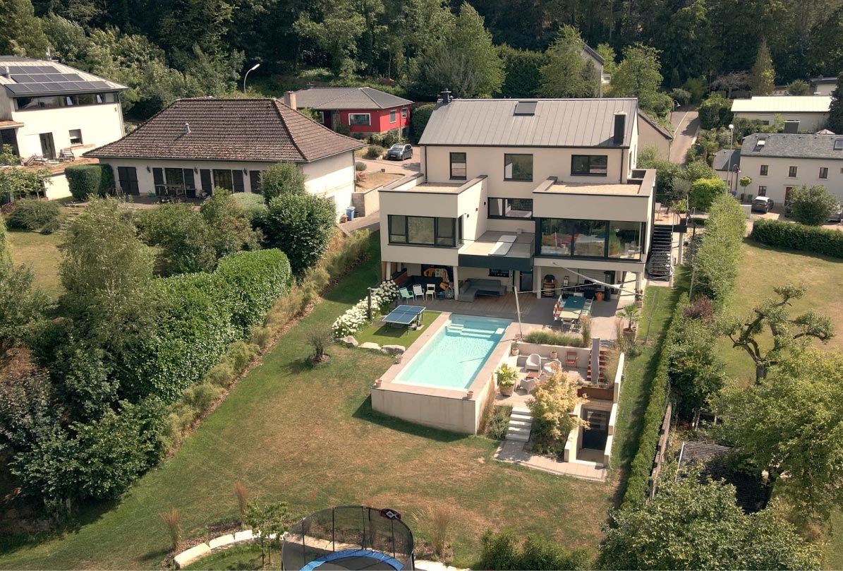 Ein modernes zweistöckiges Haus mit einem Pool im Hinterhof, Sitzgelegenheiten im Freien und einem wunderschön gestalteten Gartenbereich von Garten- und Landschaftsbau zeigt an einem sonnigen Tag elegantes Gardendesign in einer Wohngegend.
