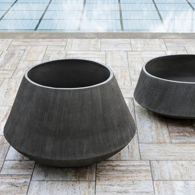 Zwei große, moderne Burelbach-Pflanzgefäße aus Beton mit breiten Öffnungen stehen auf einer hellen, gemusterten Steinterrasse neben einem gefliesten, spiegelnden Pool und verleihen Ihrem Gardendesign dezente Eleganz.