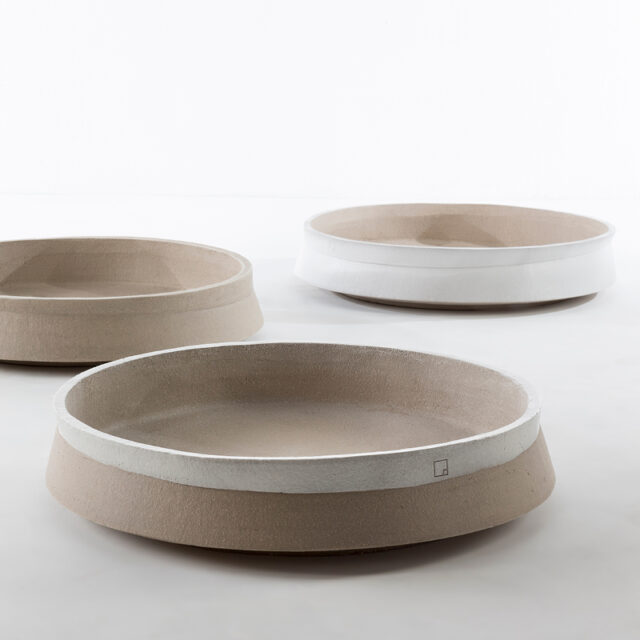 Drei breite, flache, runde Keramikschalen mit minimalistischem Design sind auf einer weißen Fläche angeordnet. Die glatte Textur und die erdigen Töne jeder Schale inspirieren Gardendesign und Handwerk in modernen Interieurs.