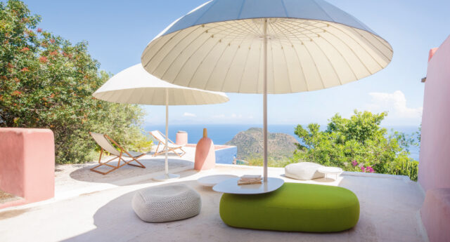 Terrasse in Luxemburg mit Outdoormöbeln, Loungesesseln, großen weißen Sonnenschirmen und einem Blick auf das Meer unter blauem Himmel.