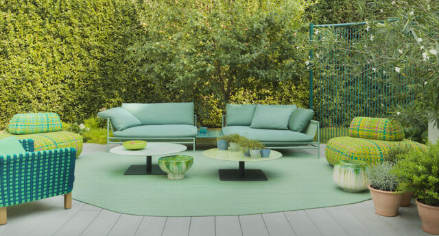 Moderne Außenterrasse mit grünen Sofas, gemusterten Stühlen, runden Tischen und Topfpflanzen auf einer Holzterrasse, mit stilvollen Outdoormöbeln, die sich ideal für Gartenbauprojekte eignen.