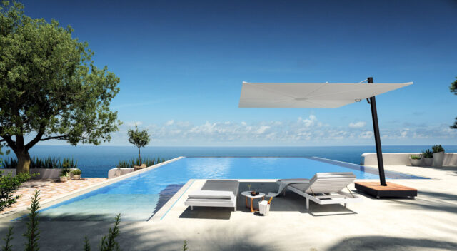 Ein moderner Infinity-Pool von Burelbach bietet einen Blick auf den Ozean unter einem strahlend blauen Himmel. Zwei Liegestühle und ein Tisch stehen unter einem großen weißen Sonnenschirm, umgeben von einer vom Gardendesign inspirierten Bepflanzung und einer minimalistischen Landschaftsgestaltung.