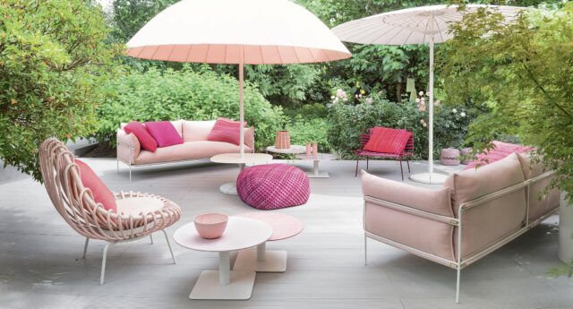 Eine Außenterrasse mit rosa Sofas, Tischen, Sonnenschirmen und Kissen, umgeben von grünen Pflanzen und Bäumen, mit stilvollen Outdoormöbeln, die in Luxemburg und Deutschland beliebt sind.