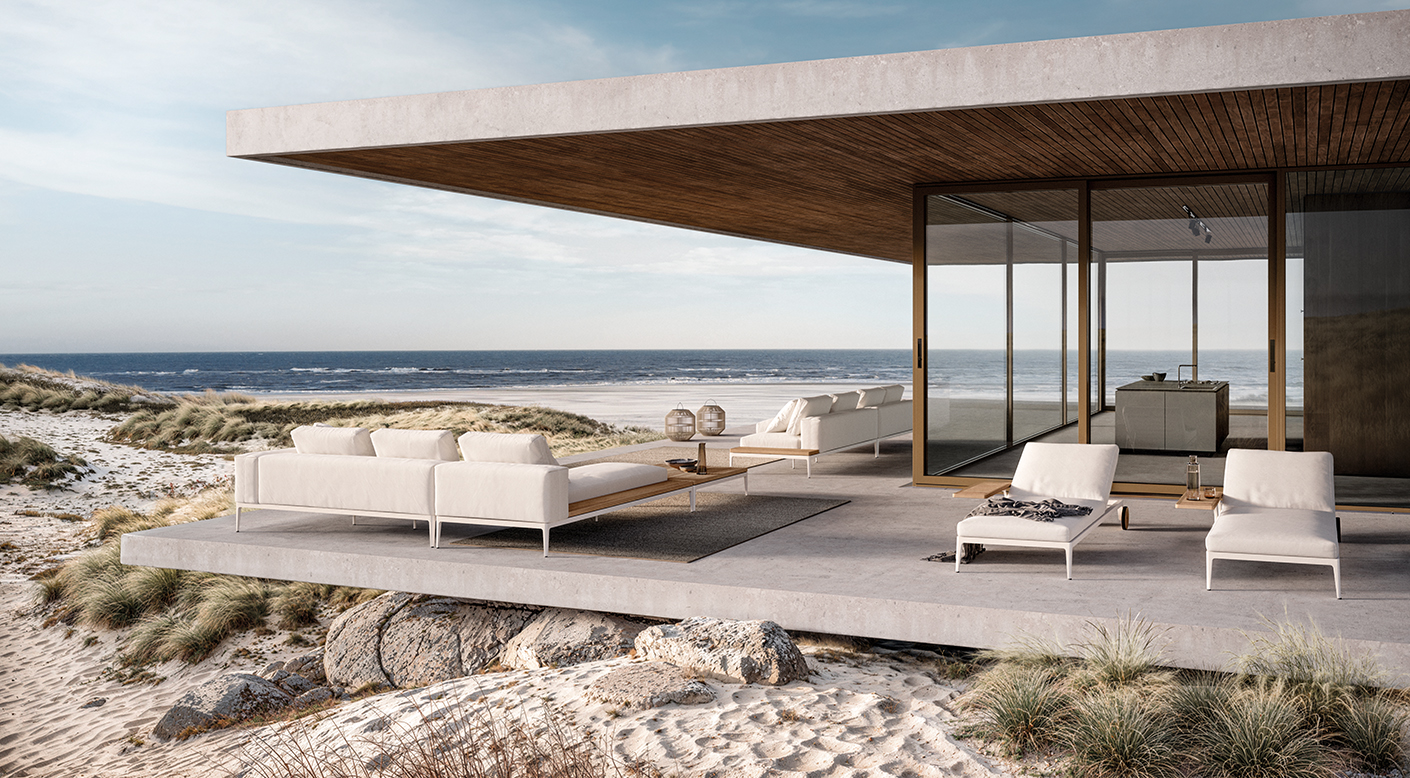 Ein modernes Strandhaus mit raumhohen Glaswänden, einer Holzdecke und einer mit weißen Outdoor-Sofas ausgestatteten Betonterrasse unterstreicht den eleganten Garten- und Landschaftsbau, der von Küstenstilen aus Deutschland und Luxemburg inspiriert ist.
