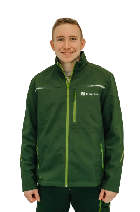 Ein lächelnder junger Mann in einer dunkelgrünen Jacke mit gelben Reißverschlüssen und dem BURELBACH-Logo steht vor einem weißen Hintergrund - bereit, Ihr nächstes Projekt mit Gardendesign-Know-how und handwerklichem Geschick zu unterstützen.