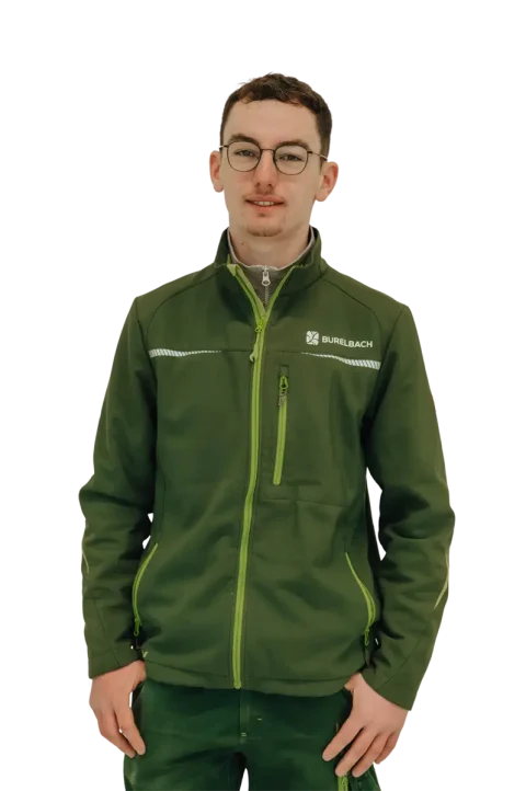 Ein junger Mann mit kurzen Haaren und Brille trägt eine grüne Jacke der Marke Burelbach und eine dazu passende Hose. Er steht vor einem weißen Hintergrund und schaut in die Kamera - eine dezente Anspielung auf den modernen Gardendesign-Stil.