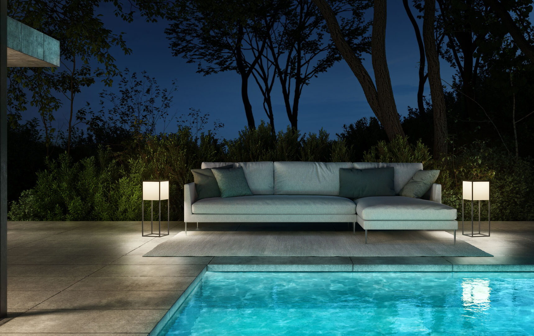 Eine moderne Terrasse bei Nacht mit Burelbach Gartenmöbeln, einem Sektionssofa mit Kissen, zwei beleuchteten Stehlampen auf beiden Seiten und einem leuchtenden Pool im Vordergrund, umgeben von Bäumen und Sträuchern für ein atemberaubendes Gardendesign.