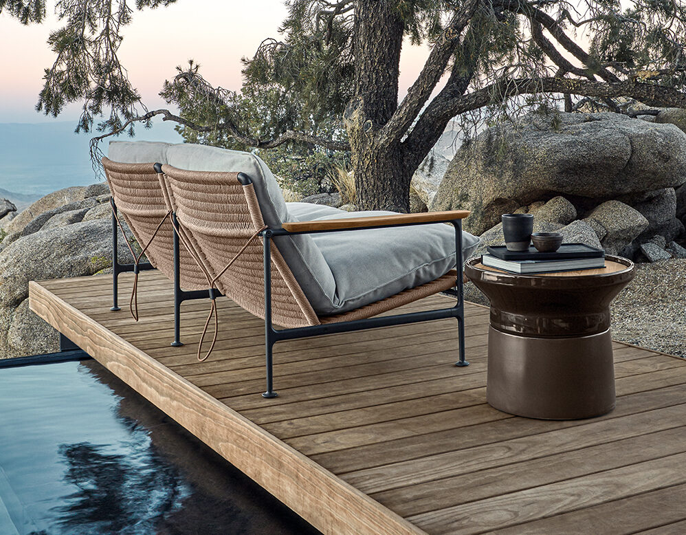 Zwei gepolsterte Loungesessel auf einem Holzdeck blicken auf eine felsige Landschaft mit Bäumen - ein einladendes Beispiel für Gartendesign in Deutschland und Luxemburg. Ein kleiner Tisch mit Tassen und einer Teekanne steht am Rande des Pools und trägt zur Entspannung im Freien bei.