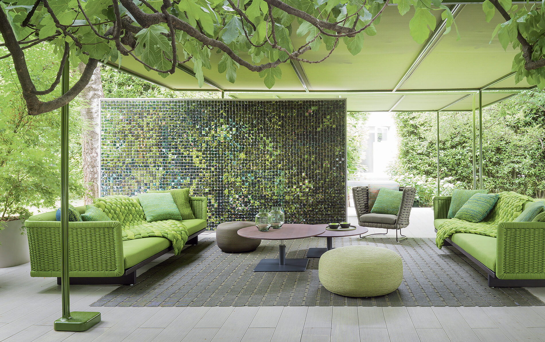 Moderne Outdoor-Lounge mit grünen Sofas, Blätterdach, Mosaikwand und modernen Outdoormöbeln in einer stilvollen Gartenbau-Umgebung.