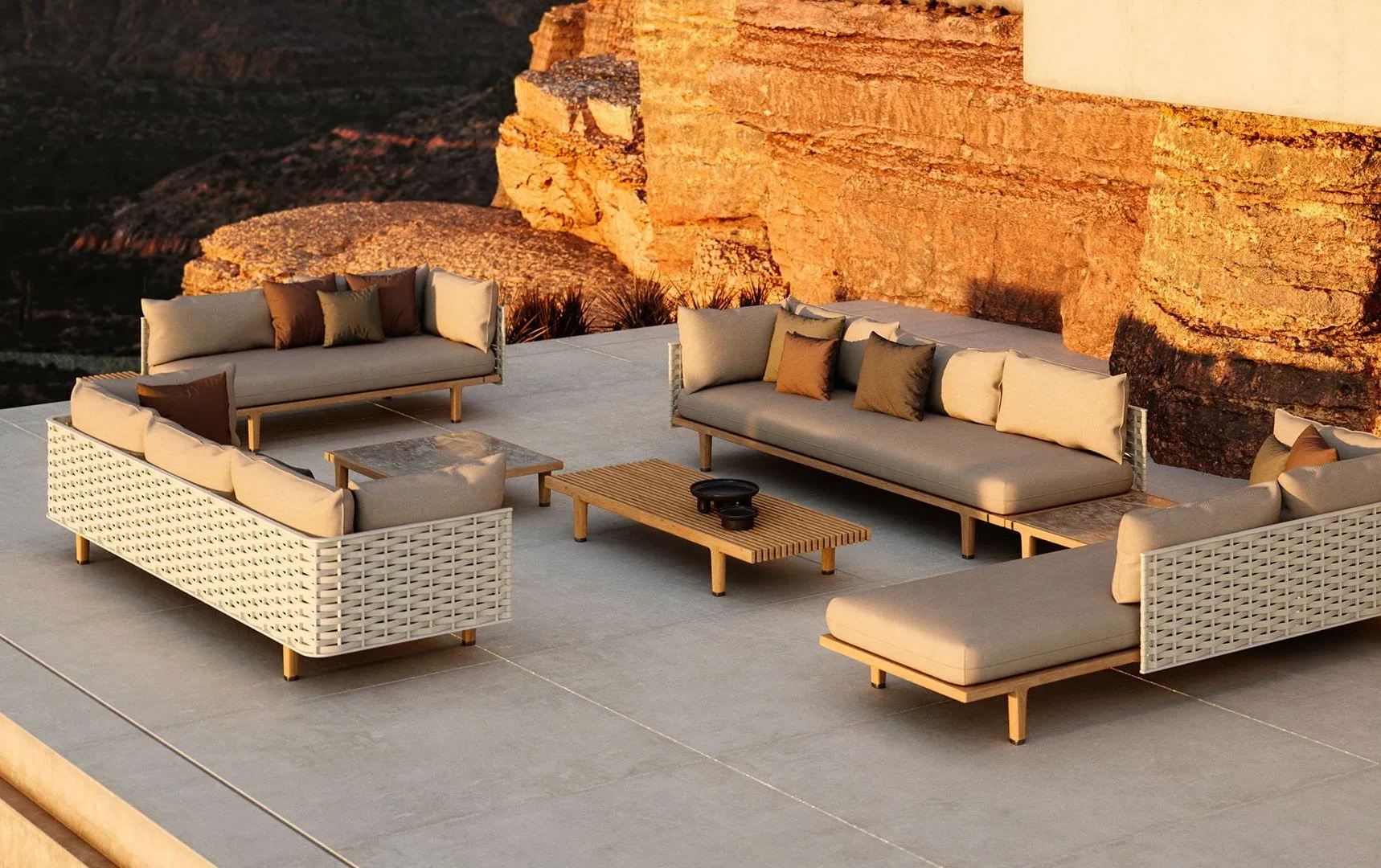 Moderne Outdoor-Lounge mit drei beigen Sofas, einer Holzbank und einem Couchtisch auf einer großzügigen Terrasse mit Blick auf die felsigen Klippen bei Sonnenuntergang. Elegantes Gartendesign und feines Handwerk in jedem Detail.