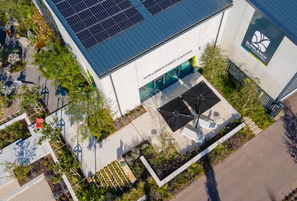 Luftaufnahme eines modernen Burelbach-Gebäudes in Luxemburg mit Sonnenkollektoren, Terrassenbestuhlung mit Outdoormöbeln und Gartenbeeten.