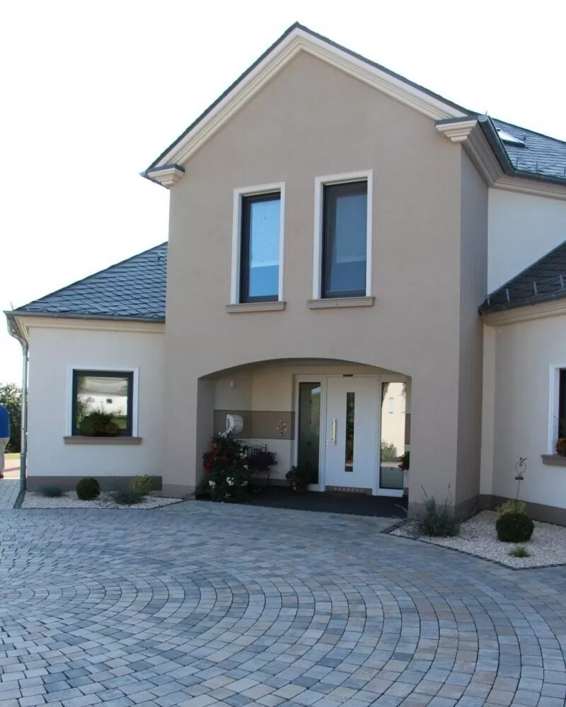 Modernes zweistöckiges beigefarbenes Haus mit bogenförmigem Eingang und gepflasterter runder Auffahrt, inspiriert von eleganten Häusern in Luxemburg und Deutschland.