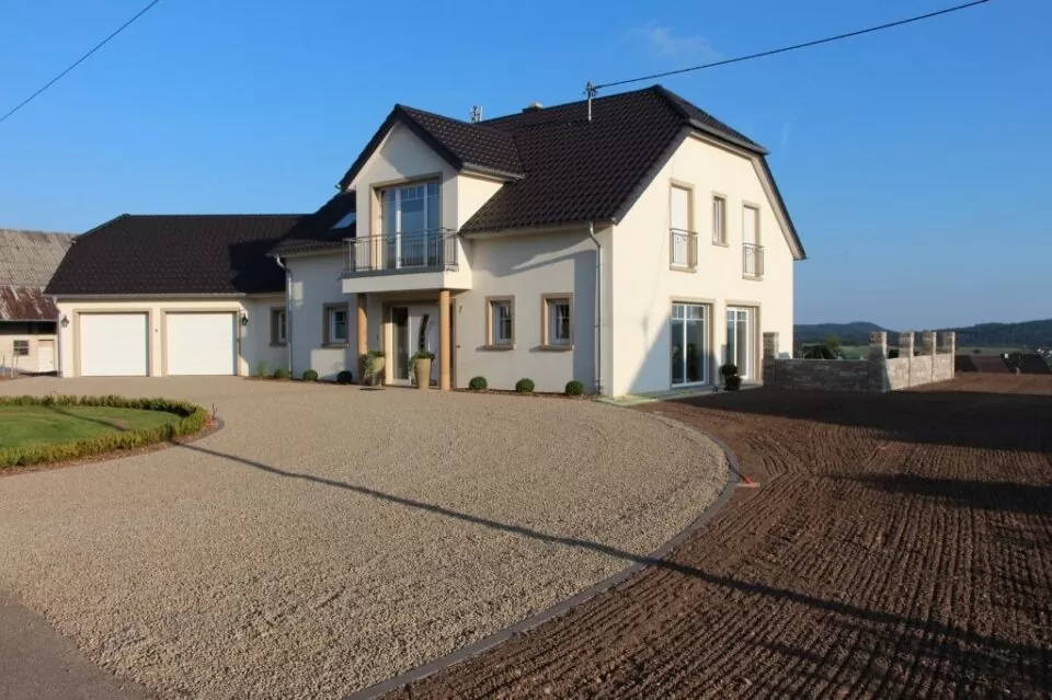 Modernes zweistöckiges Haus mit dunklem Dach und kreisförmiger Kiesauffahrt mit schönem Gartenbau, an einem klaren, sonnigen Tag.