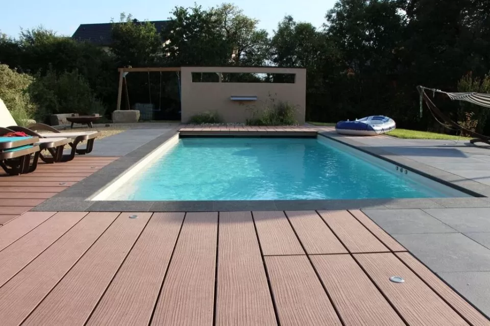 Rechteckiger Swimmingpool im Garten mit Holzdeck, Liegestühlen, Hängematte und üppigem Grün im Hintergrund; perfekt für moderne Gartengestaltung in Deutschland.