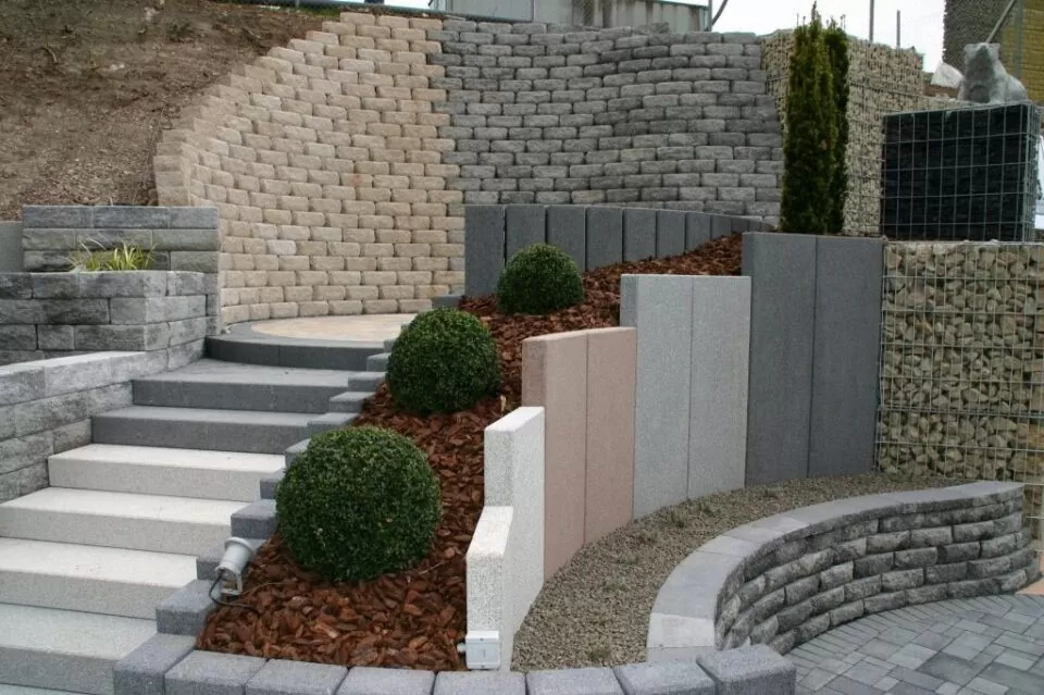 Moderner Terrassengarten in Luxemburg mit Steinstützmauern, Rundsträuchern, geschichteten Betonstufen und stilvollen Outdoormöbeln.